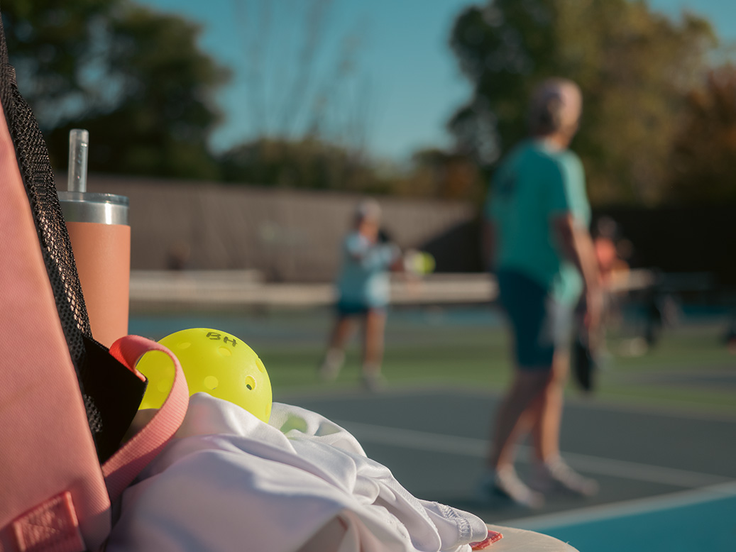 Pickleball equipment sits in the foreground as players begin a game behind. 